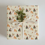 Gift wrapped in Christmas wrapping paper with corgi dogs and Christmas trees on a cream background