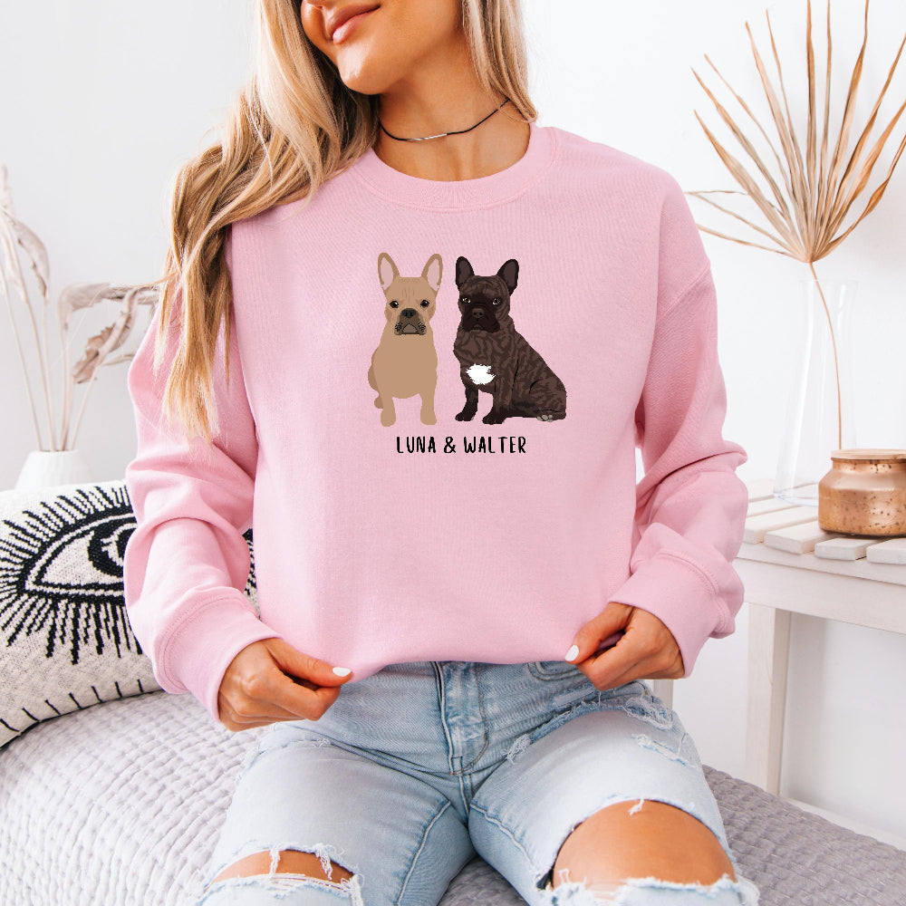 A young woman wearing a personalized French Bulldog sweatshirt  in color pink with tan frenchie and a brown frenchie, and their names underneath the dog graphic
