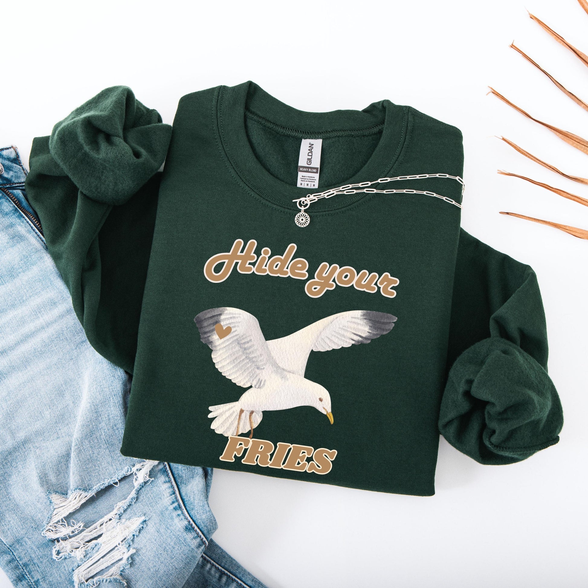 Flatlay view of a forest green colored sweatshirt with a Seagull hide your fries shirt design